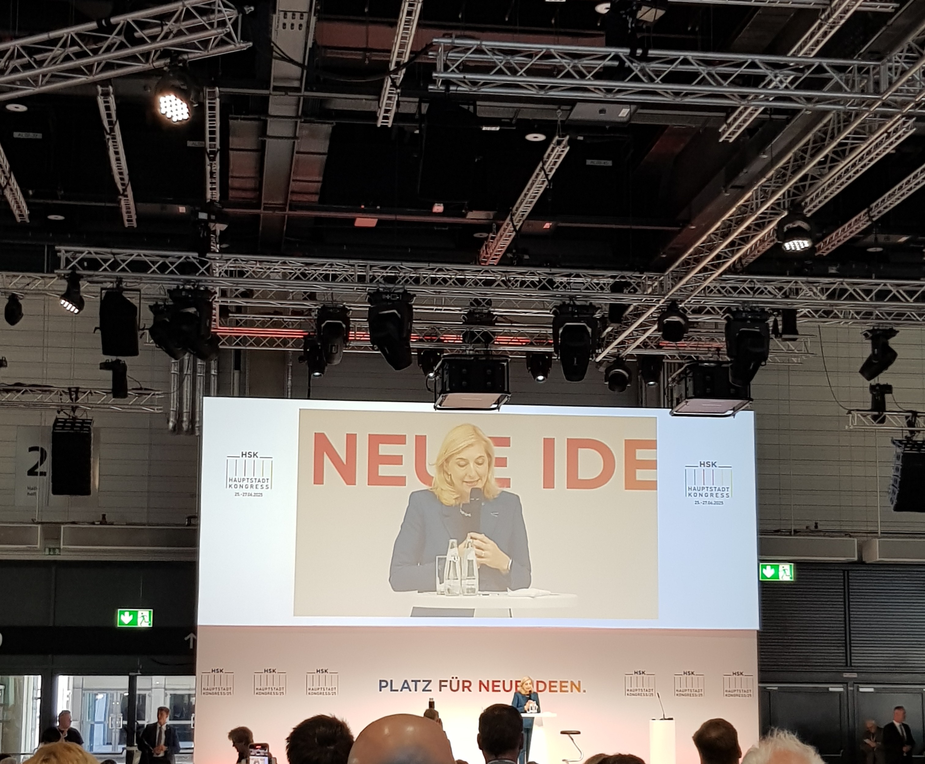 Eine LED Wand mit einer Frau, die vor einem Pult auf der Bühle spricht